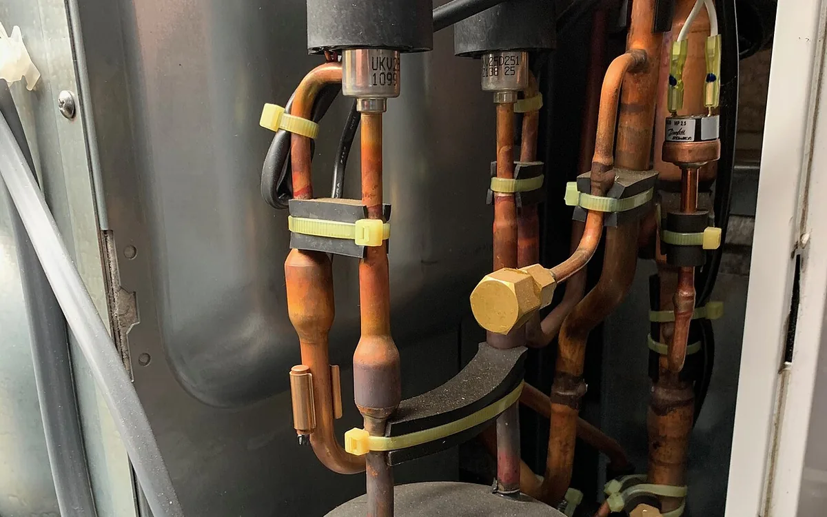 Intérieur d'une unité extérieure : compresseur, vannes et tubes de cuivre du circuit frigorifique