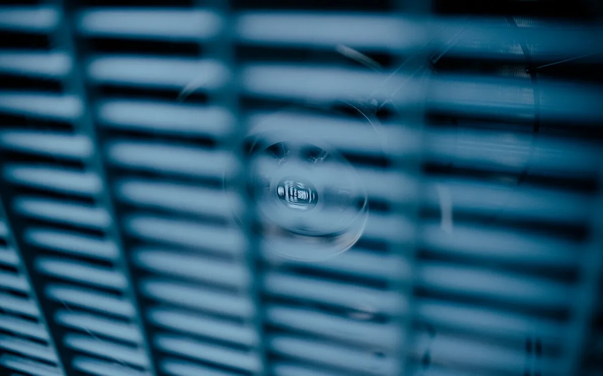 Ventilateur d'une unité extérieure en rotation, vu de près à travers sa grille de protection